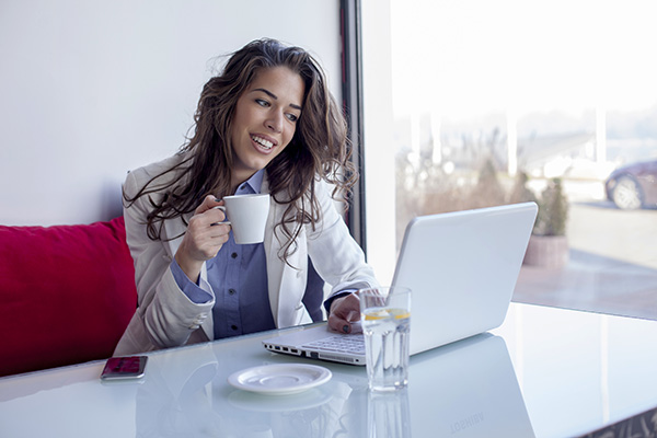 Mujer sonriente tomando un taza café por la mañana y usando una laptop Mujer sonriente tomando un taza café por la mañana y usando una laptop.